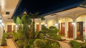Un patio de hotel con suelo de baldosas, plantas en macetas y un corredor cubierto.