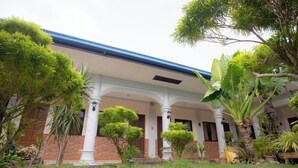 Un edificio con un patio cubierto, columnas y diversos maceteros.