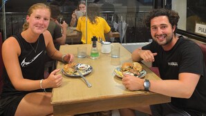 Un restaurante con una mesa de madera, dos comensales y una división de vidrio.