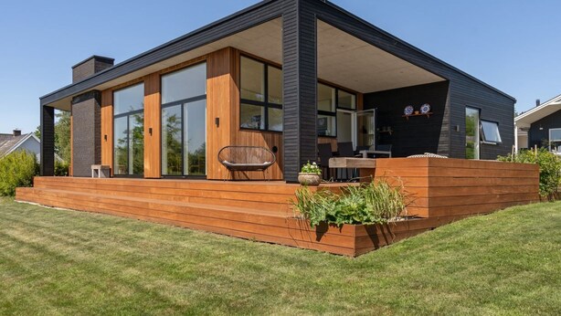 A modern house with large windows, a wooden deck, and a garden area.
