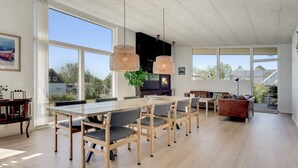 A modern kitchen with a large dining table, pendant lights, and a fireplace.