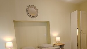 Un dormitorio con cama, mesitas de noche, armario y espejo en la pared.