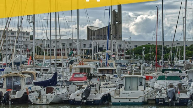 Un puerto deportivo con numerosas embarcaciones amarradas, rodeado de edificios y un cielo nublado.