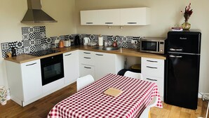 Een kleine keuken met witte kasten, een zwarte koelkast, een magnetron en een geruit tafelkleed.