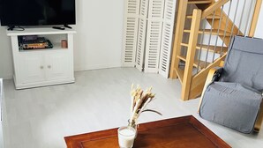 Een woonkamer met een houten salontafel, een grijze bank, een televisie op een witte kast en een trap.
