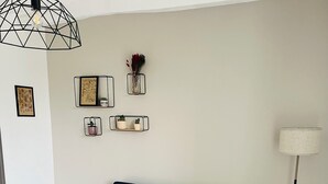 Een woonkamer met een blauwgroene bank, een houten salontafel met decoratieve items, een vloerlamp en wandplanken met ingekaderde foto's en kleine planten.