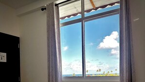 A room with a bed, two towels shaped like swans, a window with a view of the beach, and curtains.