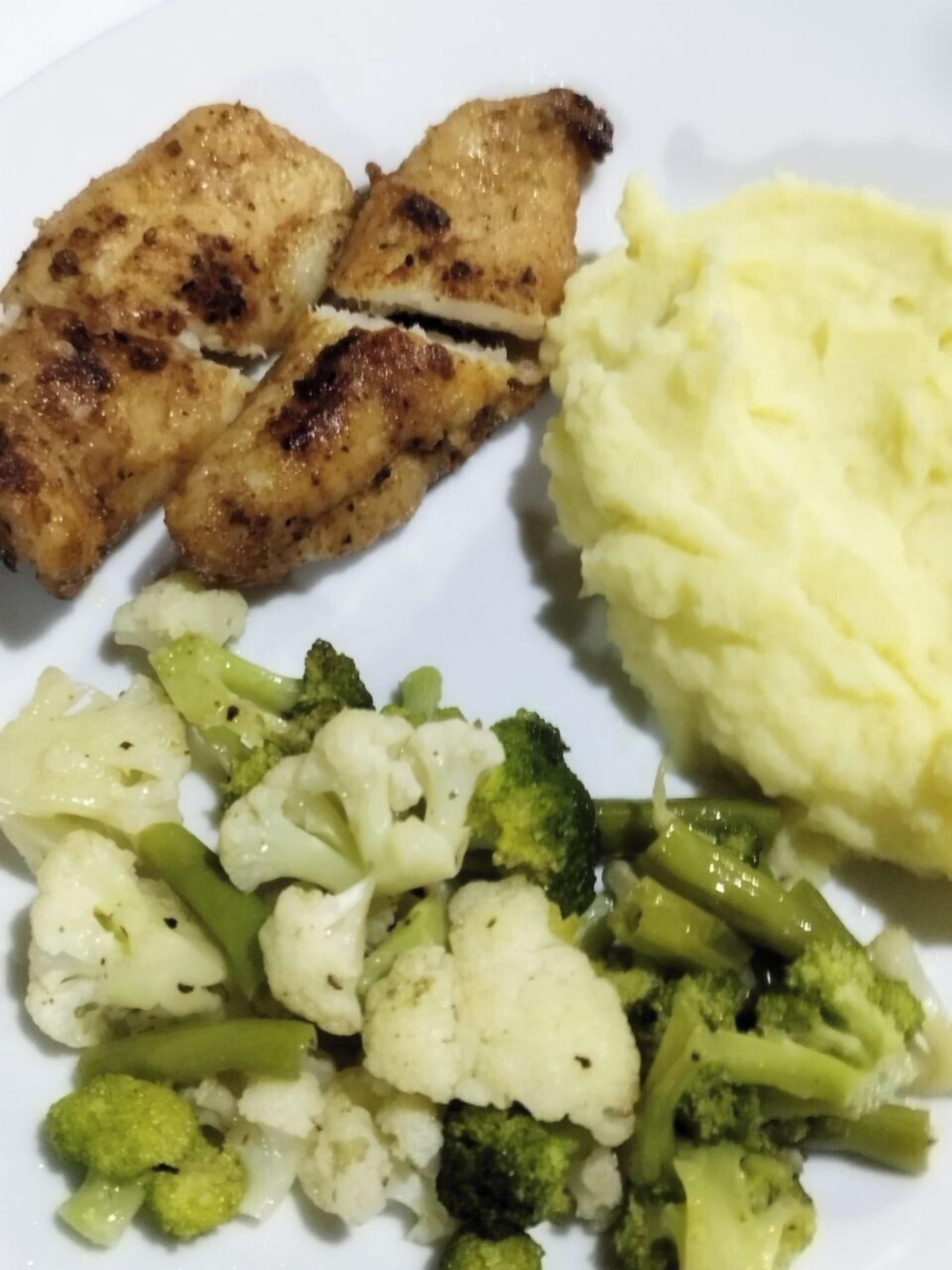 A plate with grilled chicken, mashed potatoes, and a mix of vegetables including broccoli and cauliflower.