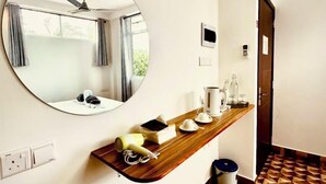 A hotel room with a round mirror, a wooden shelf with toiletries, a patterned floor, and a door leading to another room.