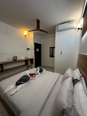Una habitación de hotel con cama, ventilador de techo, aire acondicionado, mesita de noche y espejo.