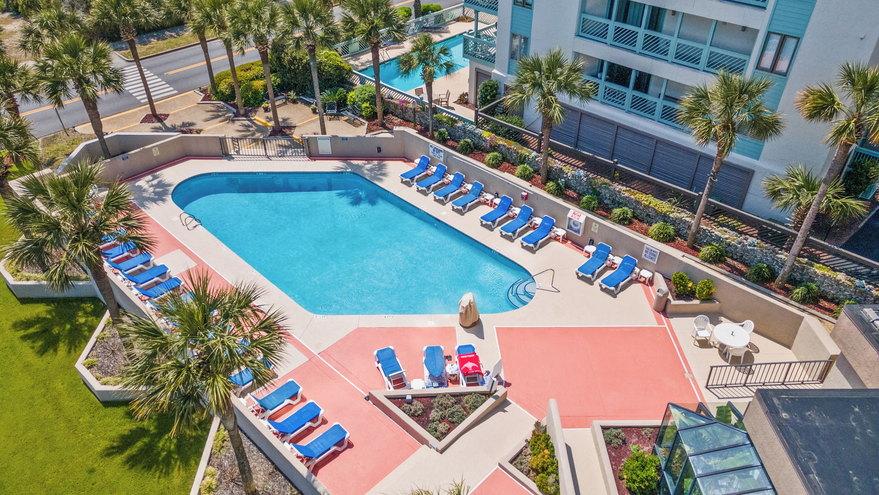 A swimming pool with sun loungers and a red deck area.
