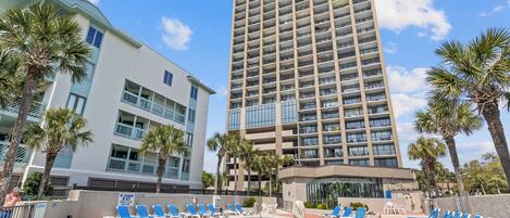 A hotel with a swimming pool, multiple floors, and palm trees.