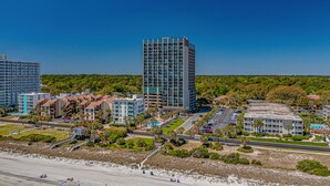 Ett hotellkomplex vid kusten med flera byggnader, inklusive ett högt huvudtorn, omgivet av grönska och en strand.