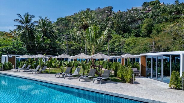A swimming pool with lounge chairs and umbrellas, surrounded by greenery and hills. - Apple House (Choeng Thale)