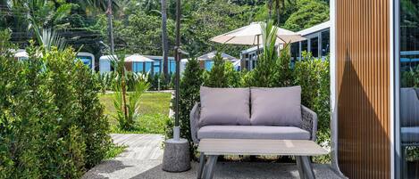A patio area with a cushioned seating arrangement, a table, and a large umbrella providing shade.