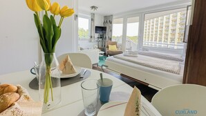 A hotel room with a dining table set for two, a bed with a view, and a balcony with a cityscape view. - Vacation apartment Watt`n Blick 220: Comfortable vacation right on the beach in Cuxhaven (Cuxhaven)