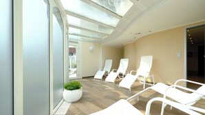 A modern waiting area with white lounge chairs, a large potted plant, and a glass door leading outside. - Vacation apartment Watt`n Blick 220: Comfortable vacation right on the beach in Cuxhaven (Cuxhaven)
