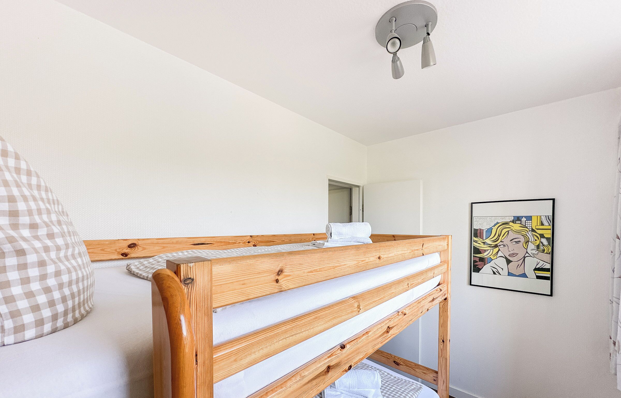 Ein Schlafzimmer mit einem Holzstockbett, einer weißen Wand, einem Deckenventilator und einem gerahmten Bild.