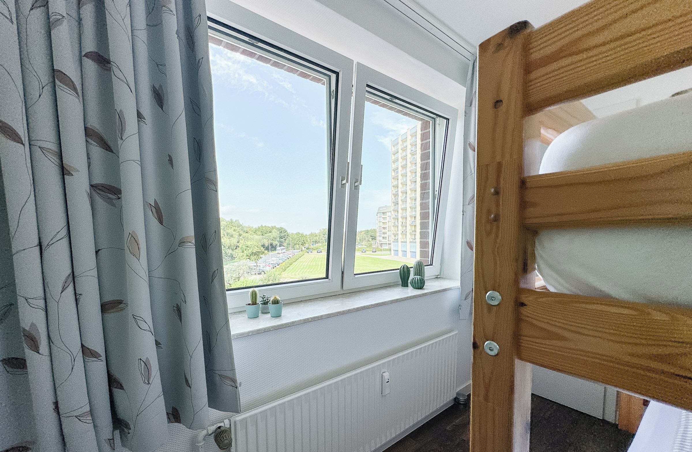 A room with a window overlooking a parking lot and buildings, a radiator, and a wooden door.
