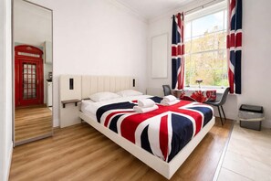 Ein Hotelzimmer mit Bett, Fenster mit Vorhängen, einem Sessel, einem kleinen Tisch und einem Papierkorb.