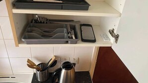 A kitchen with a countertop, a kettle, a coffee maker, a toaster, and a set of utensils on a shelf.