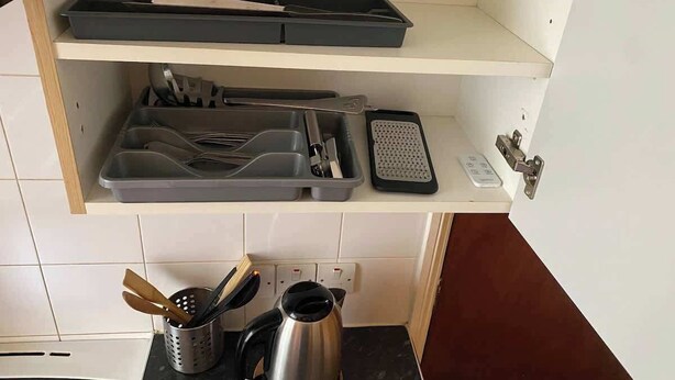 A kitchen with a countertop, a kettle, a coffee maker, a toaster, and a set of utensils on a shelf. - London Style (5) Apartment (Greater London)