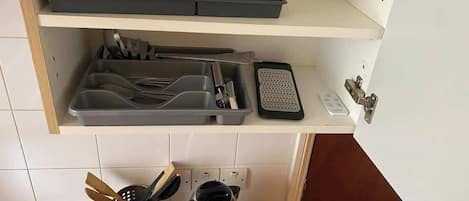 A kitchen with a countertop, a kettle, a coffee maker, a toaster, and a set of utensils on a shelf.