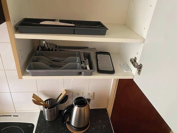 A kitchen with a countertop, a kettle, a coffee maker, a toaster, and a set of utensils on a shelf.