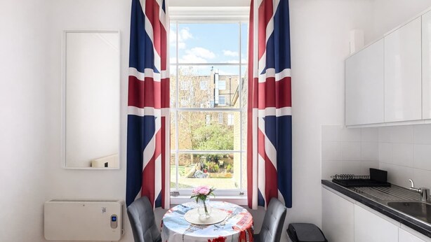 A kitchen with a window, a table with a floral tablecloth, and a view of a garden.