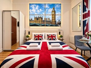 A hotel room with a large bed, a painting of Big Ben, a flag, and a small table with a glass top. - London Style (5) Apartment (Greater London)