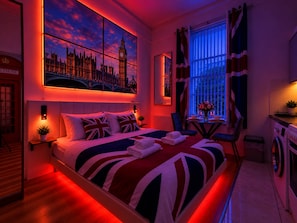 A hotel room with a large bed, a view of a famous clock tower, a small table with a vase, and a washing machine.