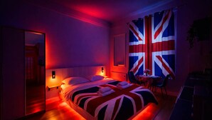 A hotel room with a bed, bedside tables, a chair, a table with a vase, and a large flag on the wall.