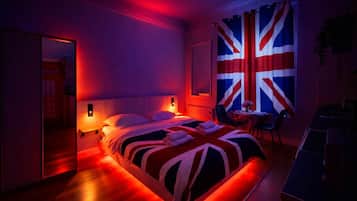 Une chambre d’hôtel avec un lit, des tables de chevet, une chaise, une table avec un vase et un grand drapeau accroché au mur.
