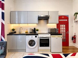 A compact kitchen with a washing machine, a microwave, a stove, and a red door labeled 'TELEPHONE'. - London Style (5) Apartment (Greater London)