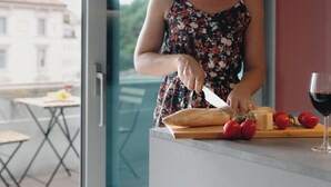 A person cutting a baguette on a wooden cutting board with tomatoes and cheese, with a glass of red wine on the table. - DONIZETTI STUDIOS (Bergamo)