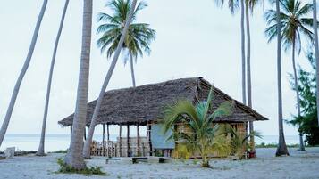 A beach hut with a thatched roof, surrounded by palm trees, and overlooking the ocean.