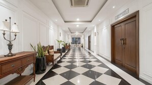 A hotel corridor with a checkered floor, wooden furniture, potted plants, and a large wooden door. - NIMS Hotel Seminyak (Seminyak)