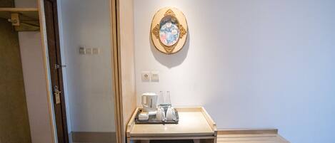 A hotel room with a wooden desk, a coffee maker, and a trash bin.