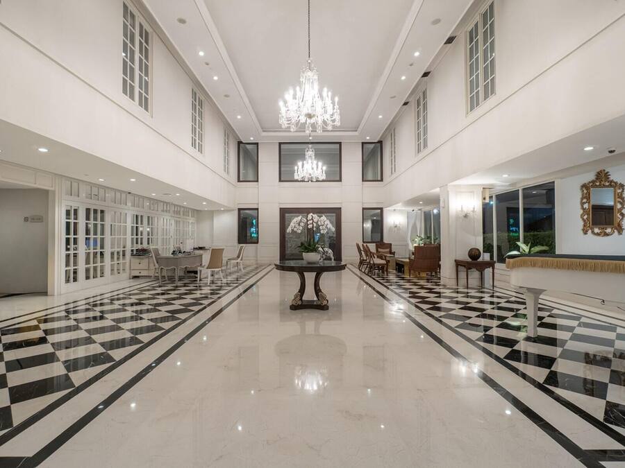 Um hall amplo com piso xadrez, um lustre central e uma área de estar com mesas e cadeiras.