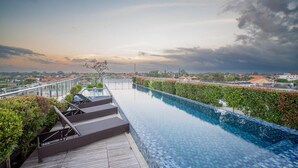 A rooftop infinity pool with a wooden deck and steps, surrounded by greenery and overlooking a cityscape. - NIMS Hotel Seminyak (Seminyak)