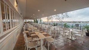 An outdoor café with white tables and chairs, a tiled floor, and a view of the cityscape. - NIMS Hotel Seminyak (Seminyak)