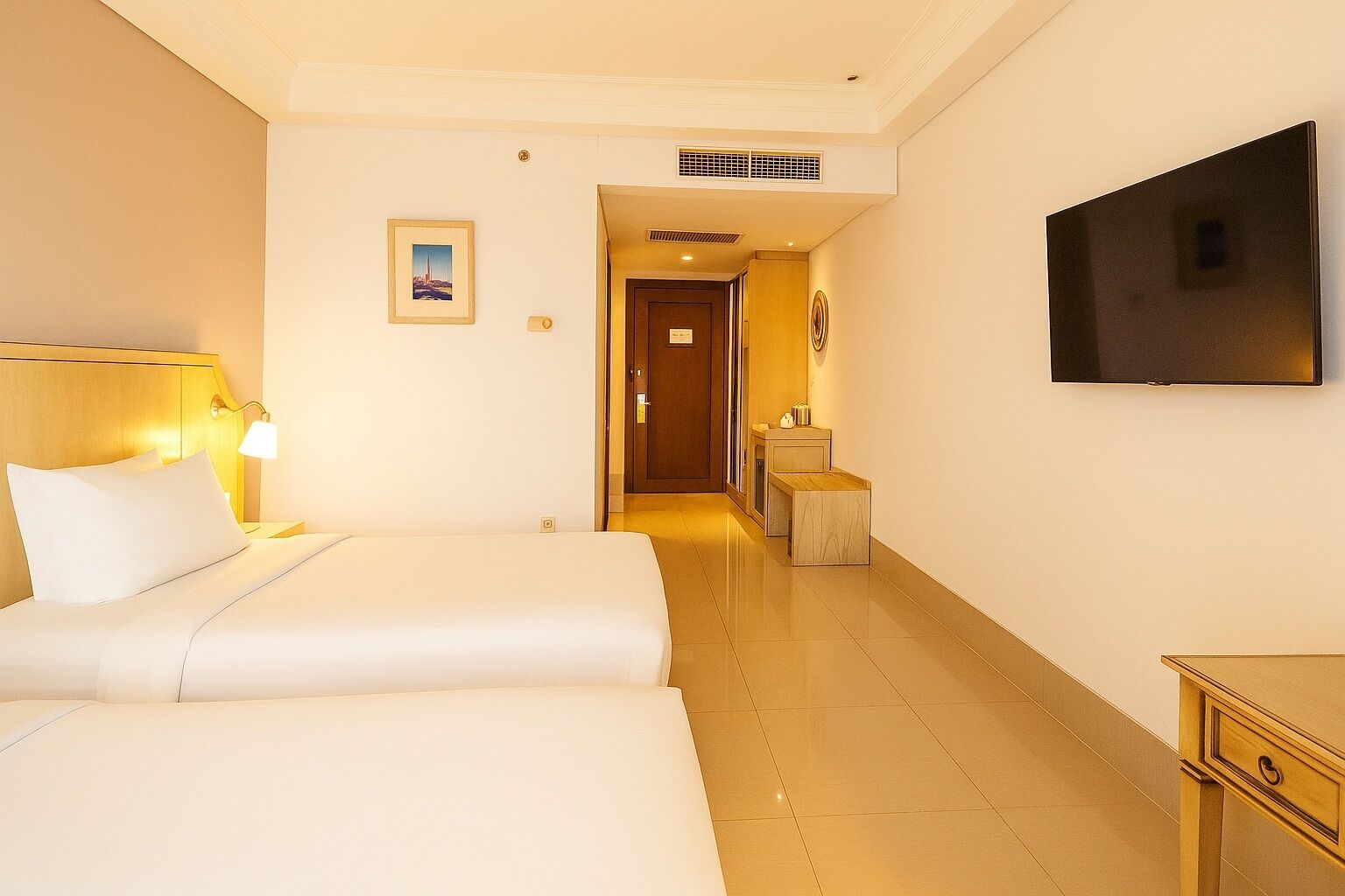 A hotel room with two beds, a TV, a picture on the wall, and a small table with a lamp.