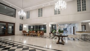 A spacious lobby with a checkered floor, a seating area with chairs and a table, and a chandelier. - NIMS Hotel Seminyak (Seminyak)