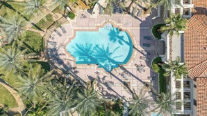 Luchtbeeld van een resort met een centraal gelegen zwembad, omringd door palmbomen en terrasjes.