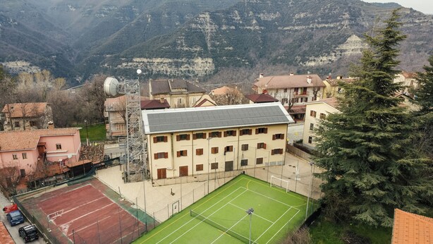 A sports facility with a tennis court, surrounded by residential buildings and mountains in the background. - Hotel Fanesia Coliving (Fano Adriano)