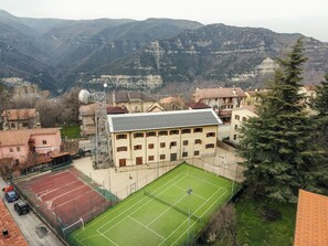 Instalación deportiva con cancha de tenis, rodeada de edificios residenciales y montañas al fondo.