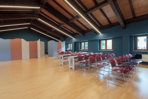 A spacious room with wooden floors and a high ceiling with exposed beams. There are multiple tables and chairs arranged for seating. - Hotel Fanesia Coliving (Fano Adriano)