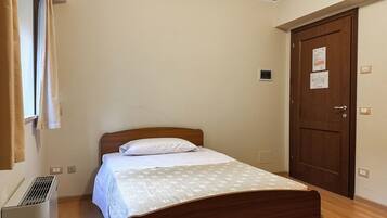 A single bed with a wooden headboard in a room with beige walls and a wooden door.