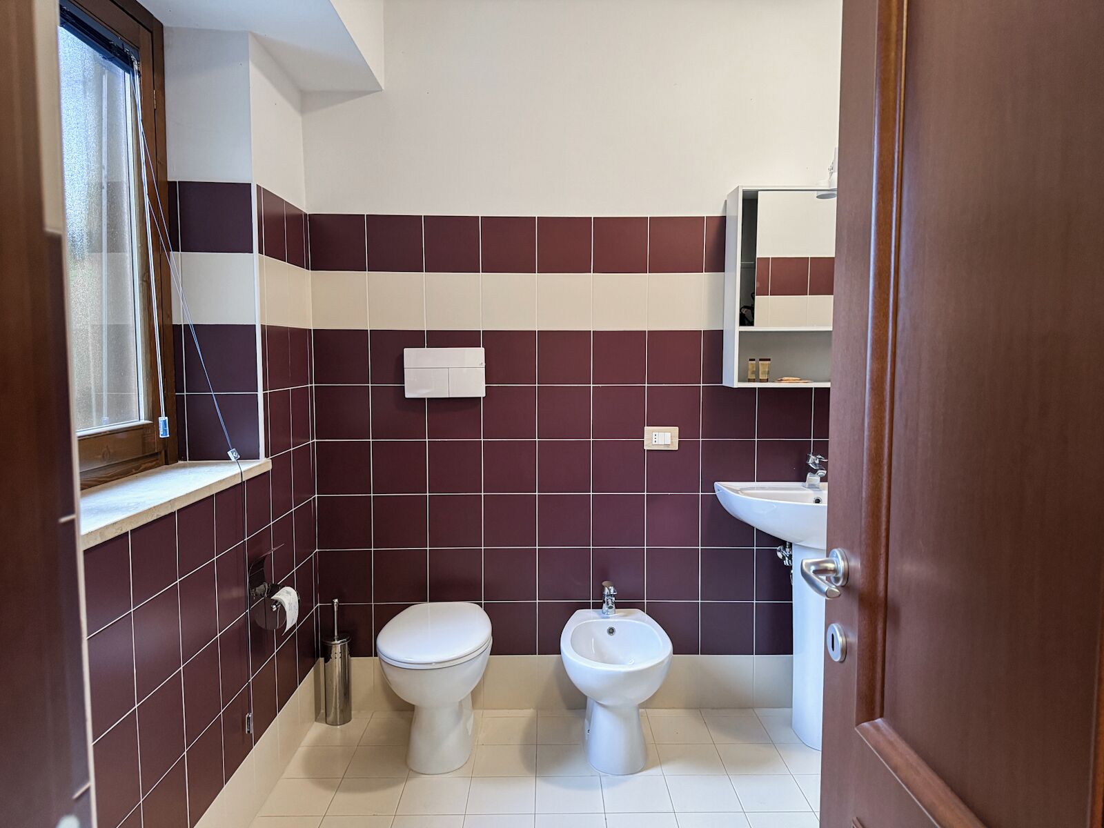 Un baño con inodoro, bidé y lavabo, con azulejos en una combinación de dos colores.