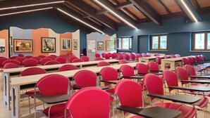 A classroom with rows of red chairs and desks, wooden beams on the ceiling, and framed artwork on the walls. - Hotel Fanesia Coliving (Fano Adriano)